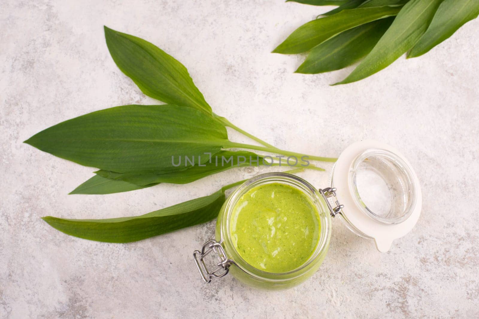 Pesto made from wild garlic, pine nuts and feta cheese in a glass, with fresh leaves on a textured background, empty space for text