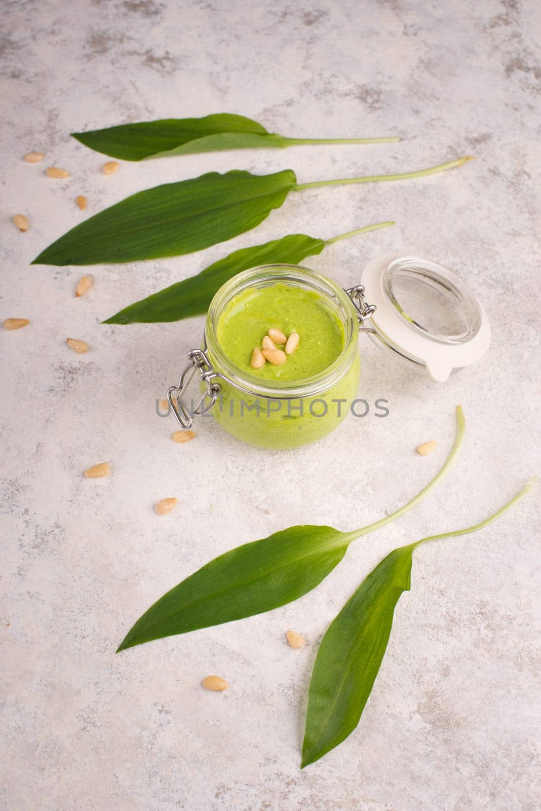 Pesto made from wild garlic, pine nuts and feta cheese in a glass, with fresh leaves on a textured background, empty space for text