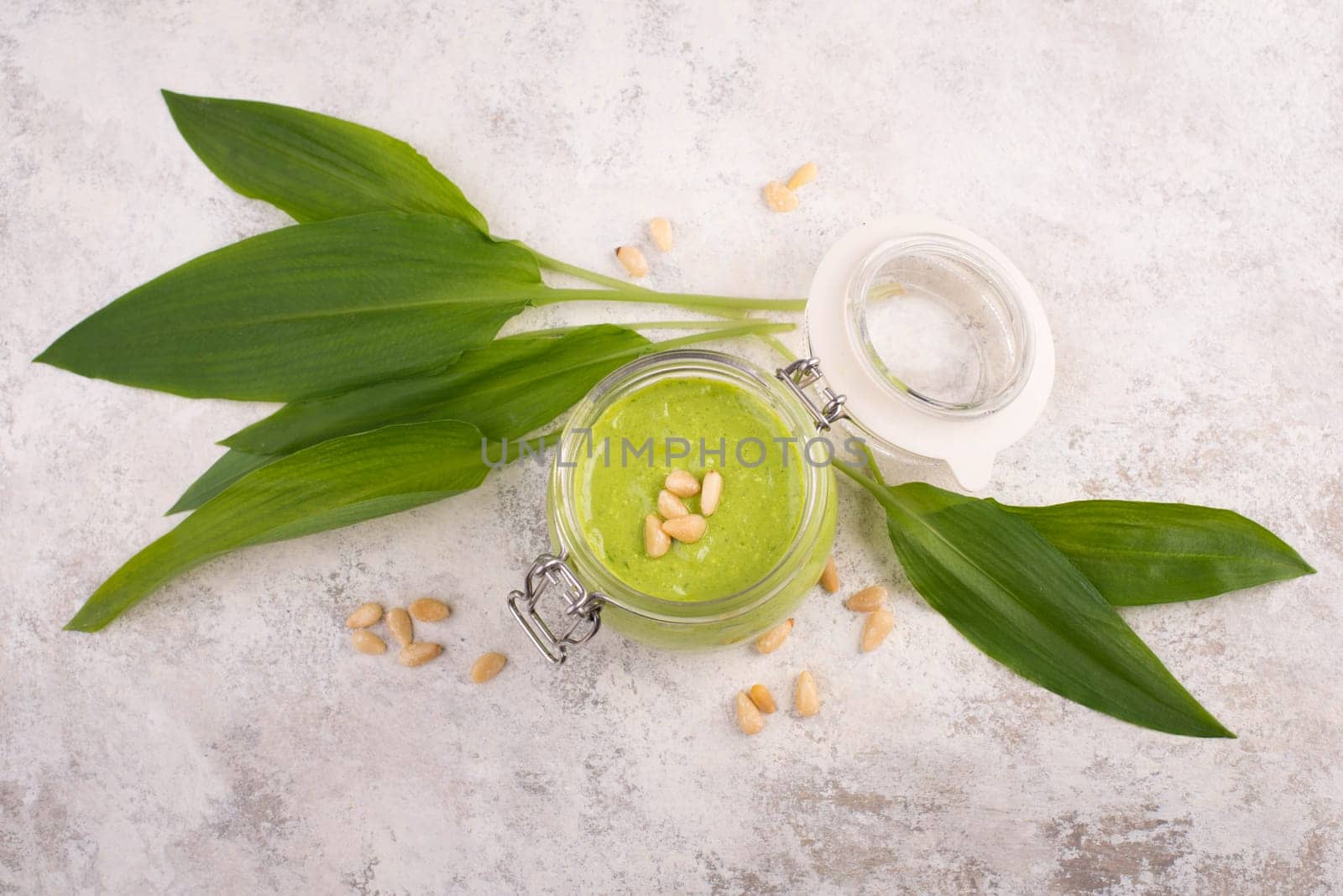 Pesto made from wild garlic, pine nuts and feta cheese in a glass, with fresh leaves on a textured background, empty space for text