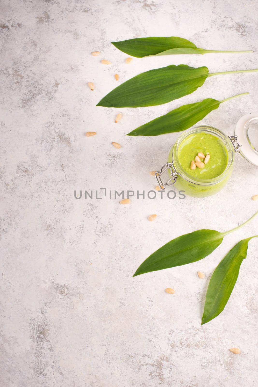 Pesto made from wild garlic, pine nuts and feta cheese in a glass, with fresh leaves on a textured background, empty space for text