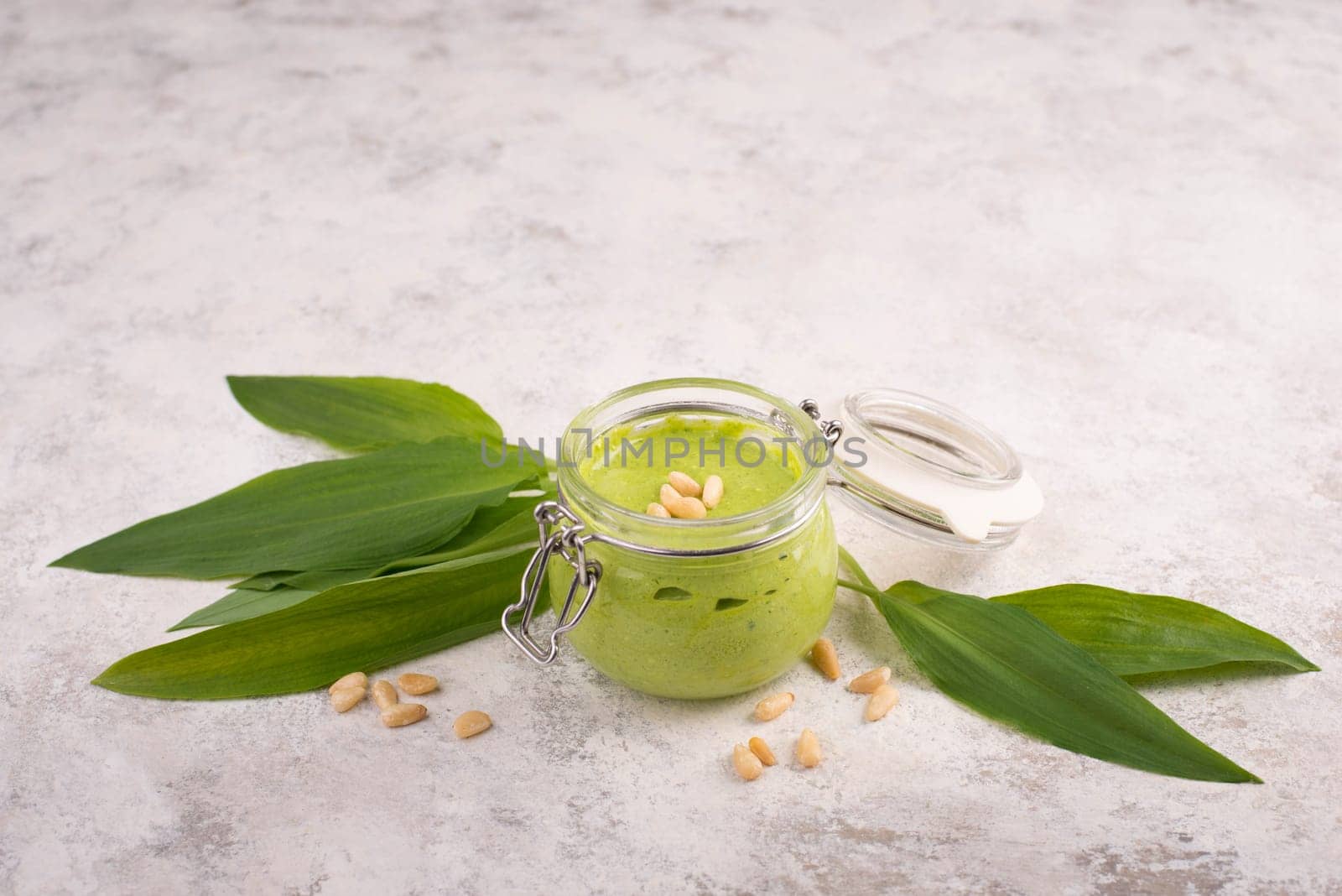 Pesto made from wild garlic, pine nuts and feta cheese in a glass, with fresh leaves on a textured background, empty space for text