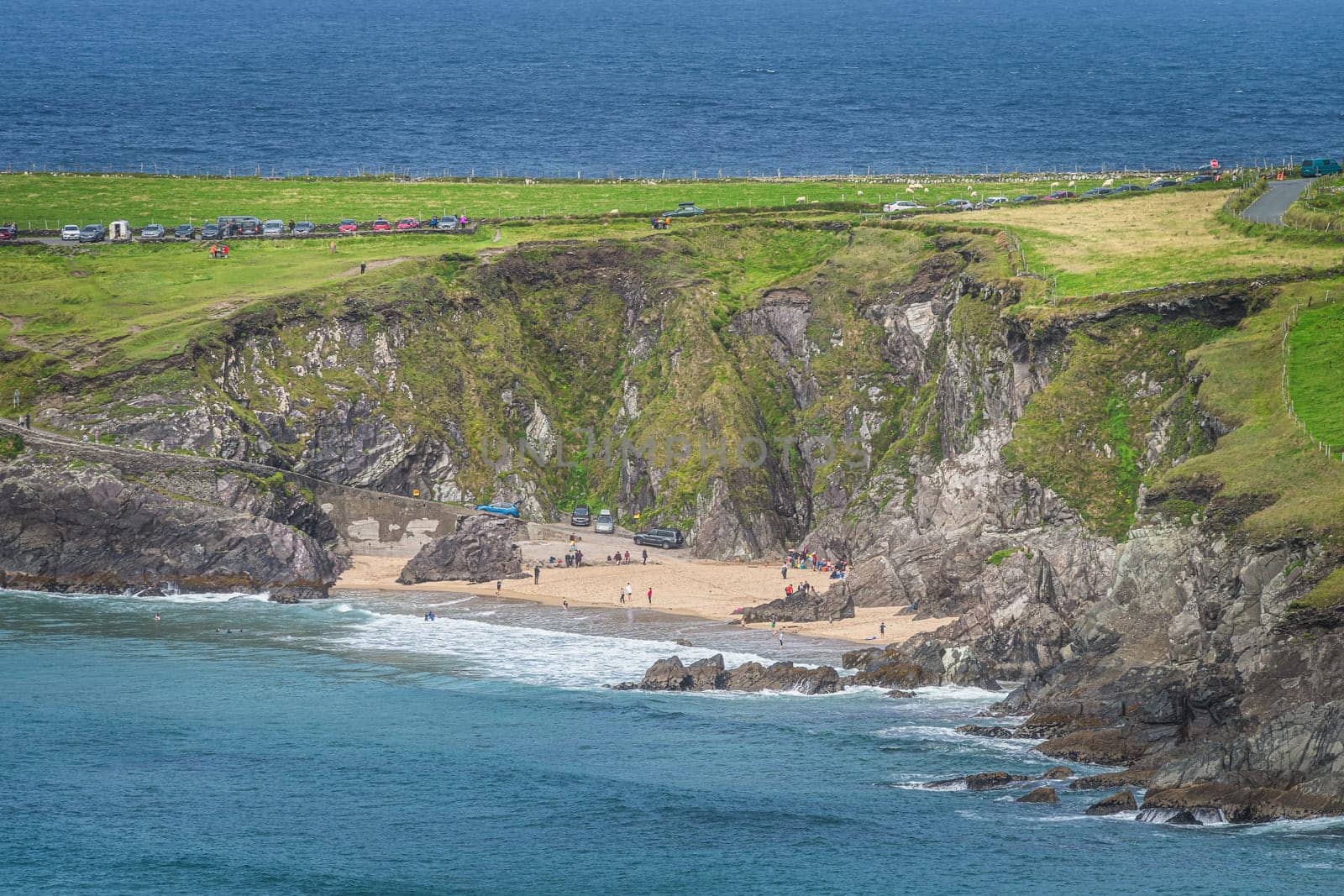 Tourist swimming in the see and relaxing on small hidden Coumeenoole Beach between cliffs in Dingle Peninsula, Wild Atlantic Way, Kerry, Ireland