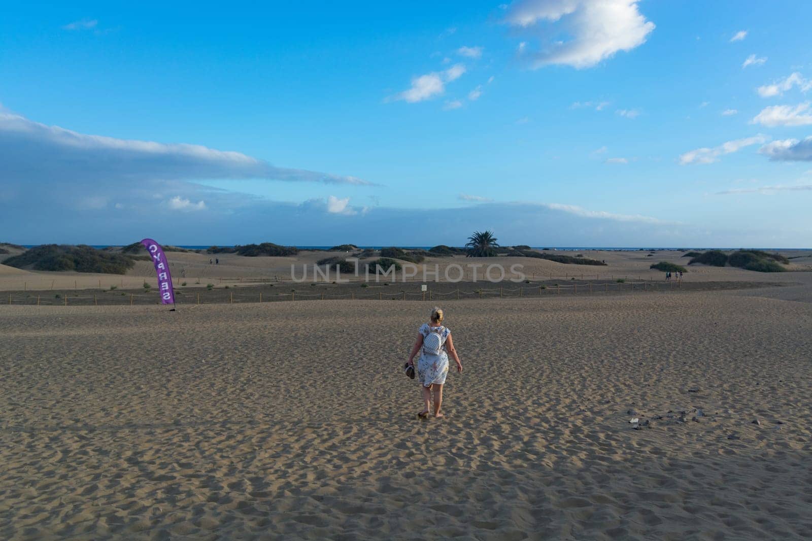 Woman in dress walking in the sand of desert dunes with steps in the desert sand, young woman walking in white sand on a bright summer day, holiday vacation concept