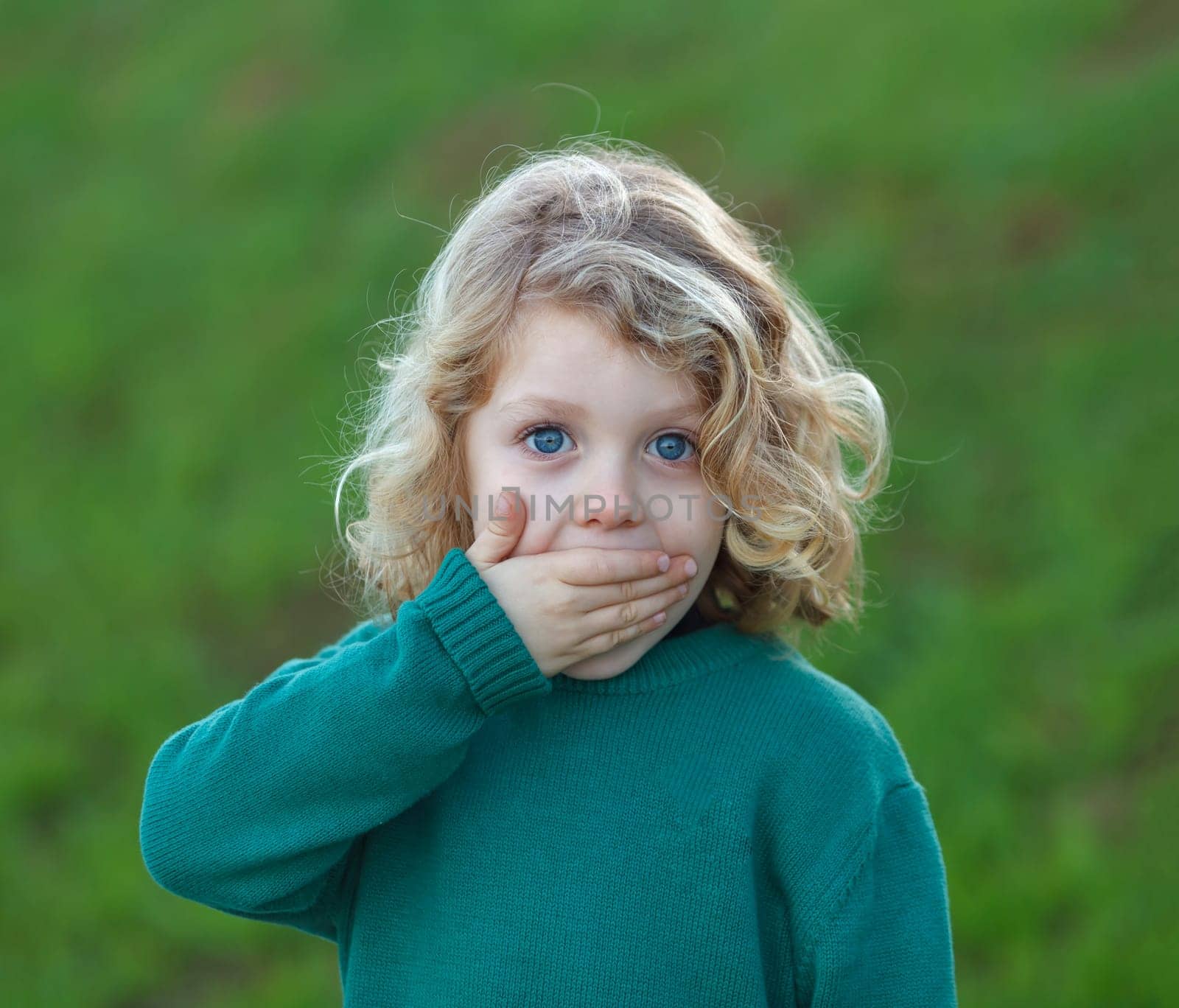 Surprised blond child with blue eyes covering his mouth