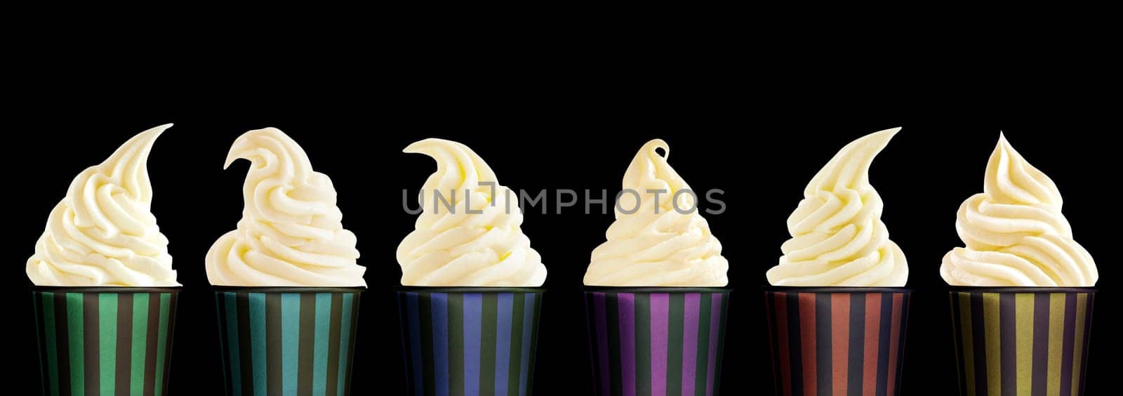 Row of six colorful striped tubs of twirled soft serve vanilla ice cream in different shapes over a black background in a panorama banner in a food styling concept