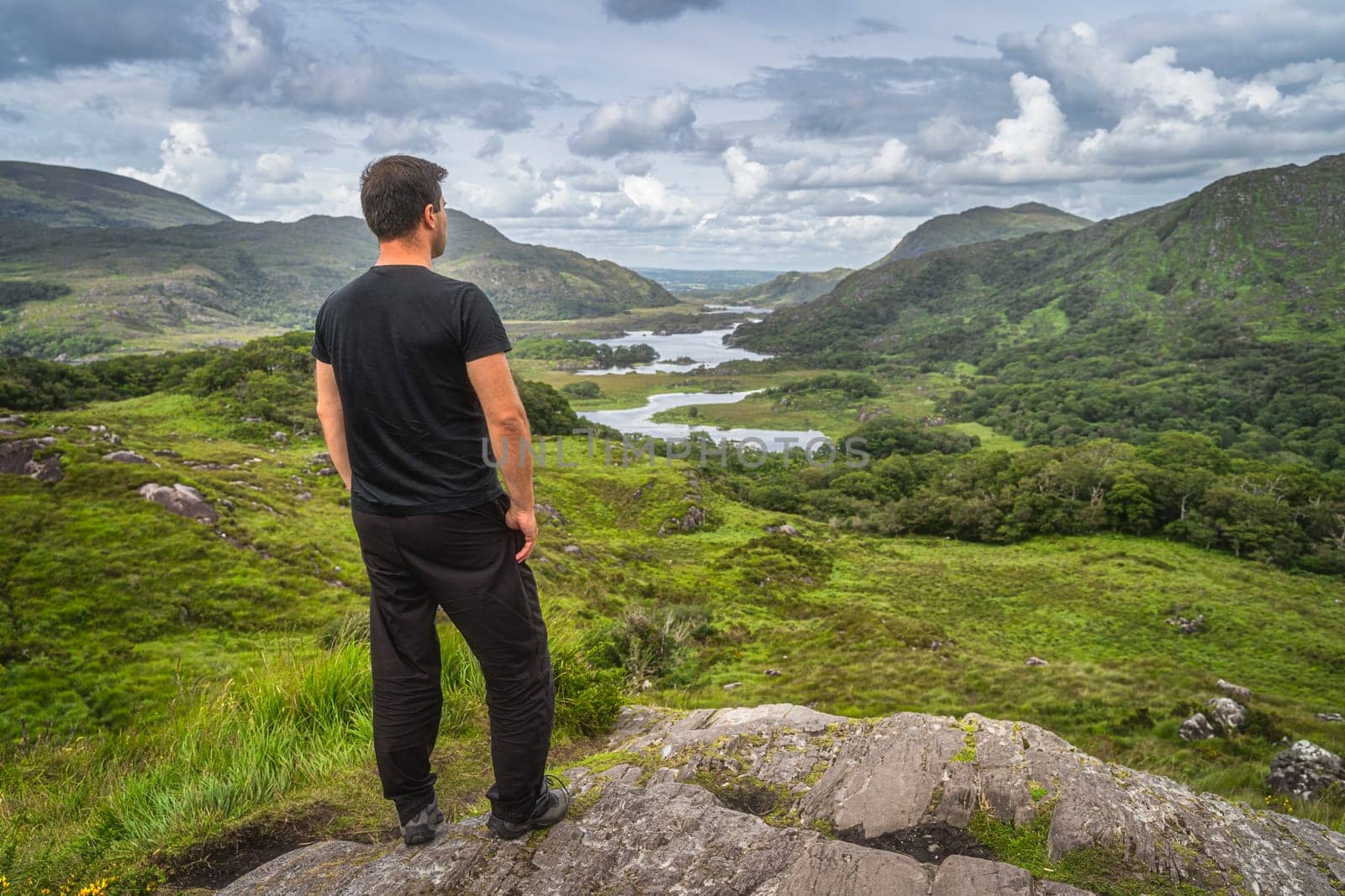 Middle age man standing on a rock and admiring beautiful Ladies View, one of iconic Irish viewpoints, Lakes of Killarney, Rink of Kerry, Ireland