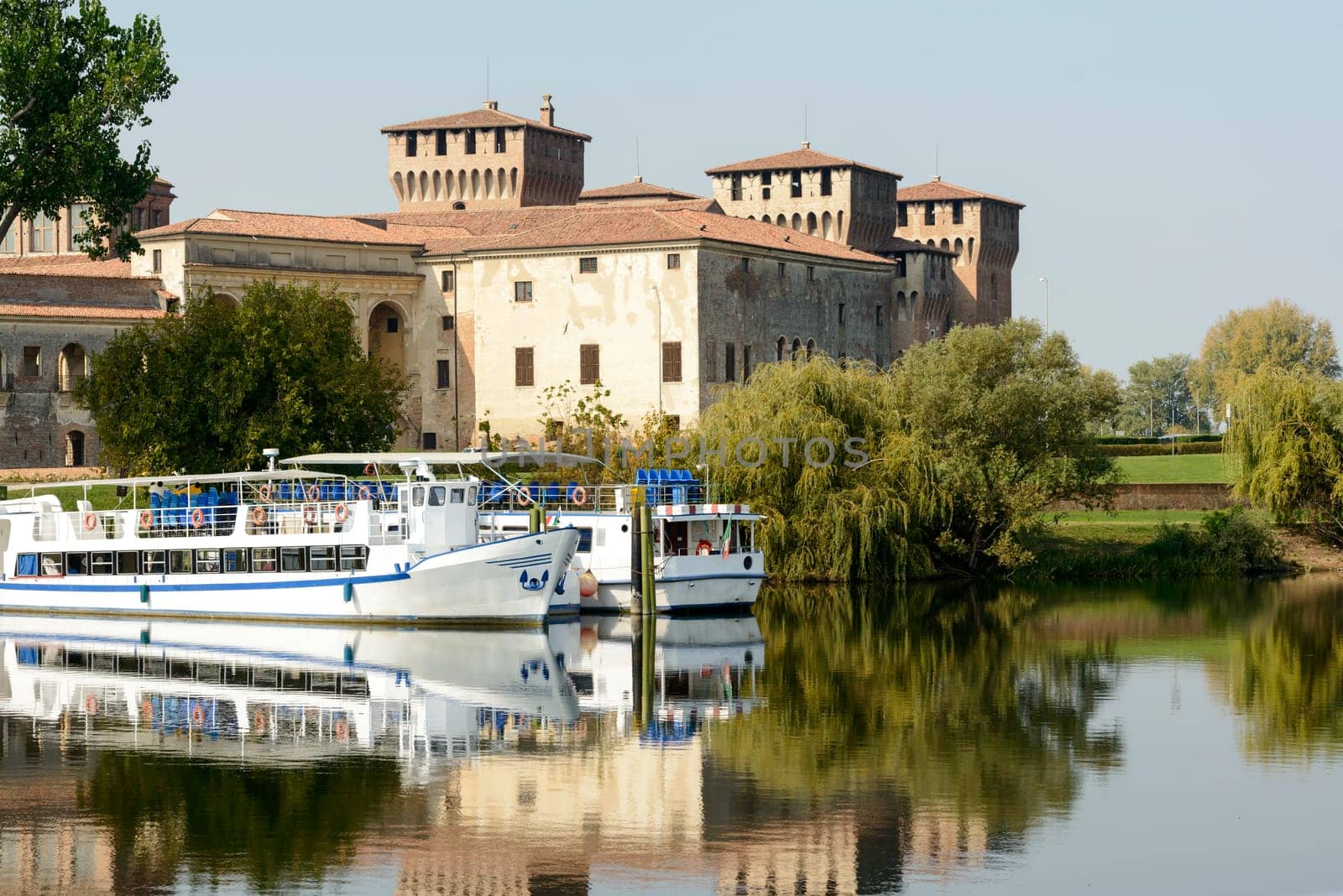 view of touristic passenger vessels and east side of Gonzaga Ducale Palace in background, shot in bright autumn sun light  at Mantua, Lombardy, Italy.