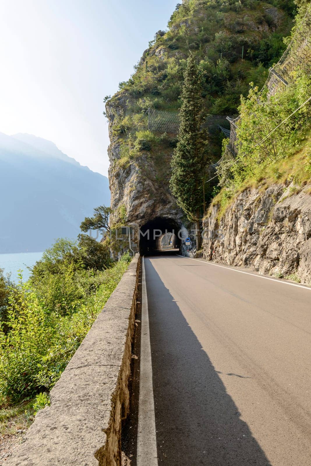 raod and tunnel under vertical rock walls on lakeside, shot in bright fall light near Limone, Brescia, Italy.