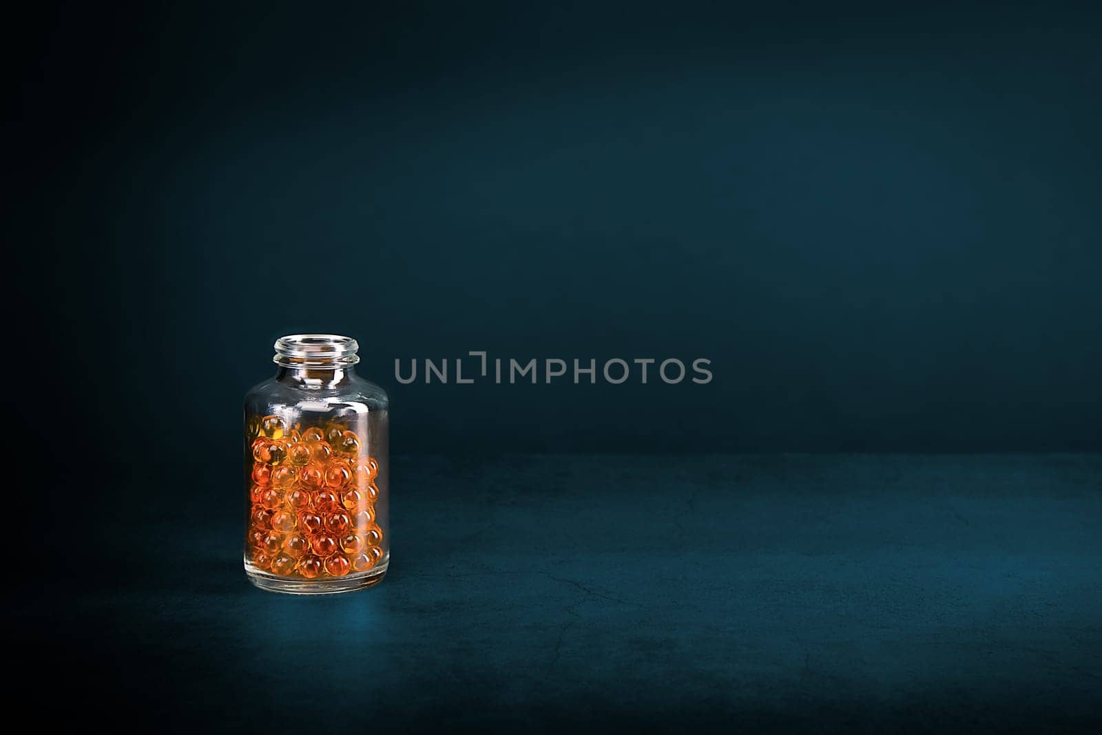 A glass jar with pills of bright orange yellow color on a blue background. Place for the label, logo, layout.