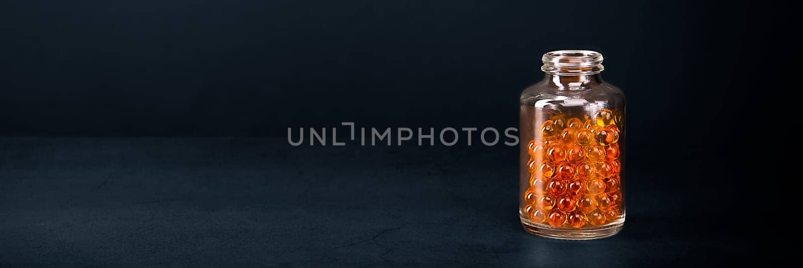 A glass jar with pills of bright orange yellow color on a blue background. Place for the label, logo, layout.