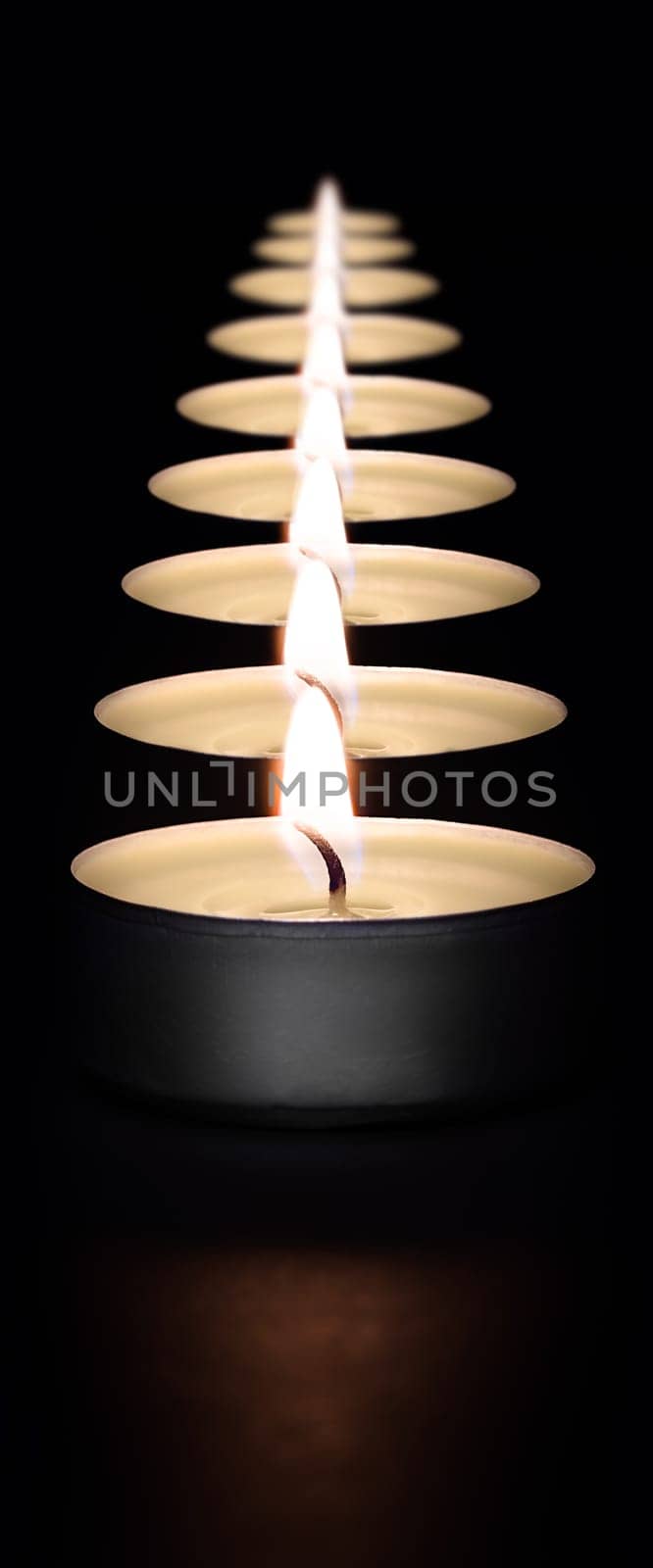 A row of burning candles on a dark background with a flare in the foreground. Layout, mockup.