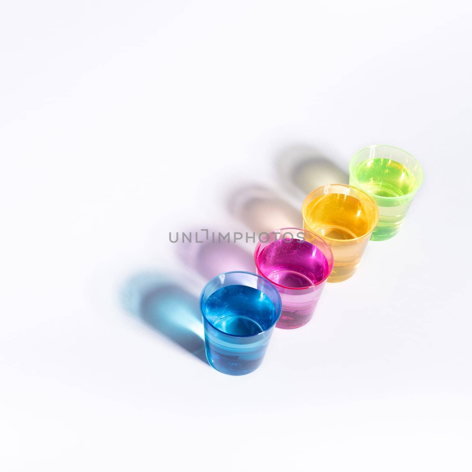 Plastic multi-colored glasses with liquid on a white background with highlights. Layout, mockup.
