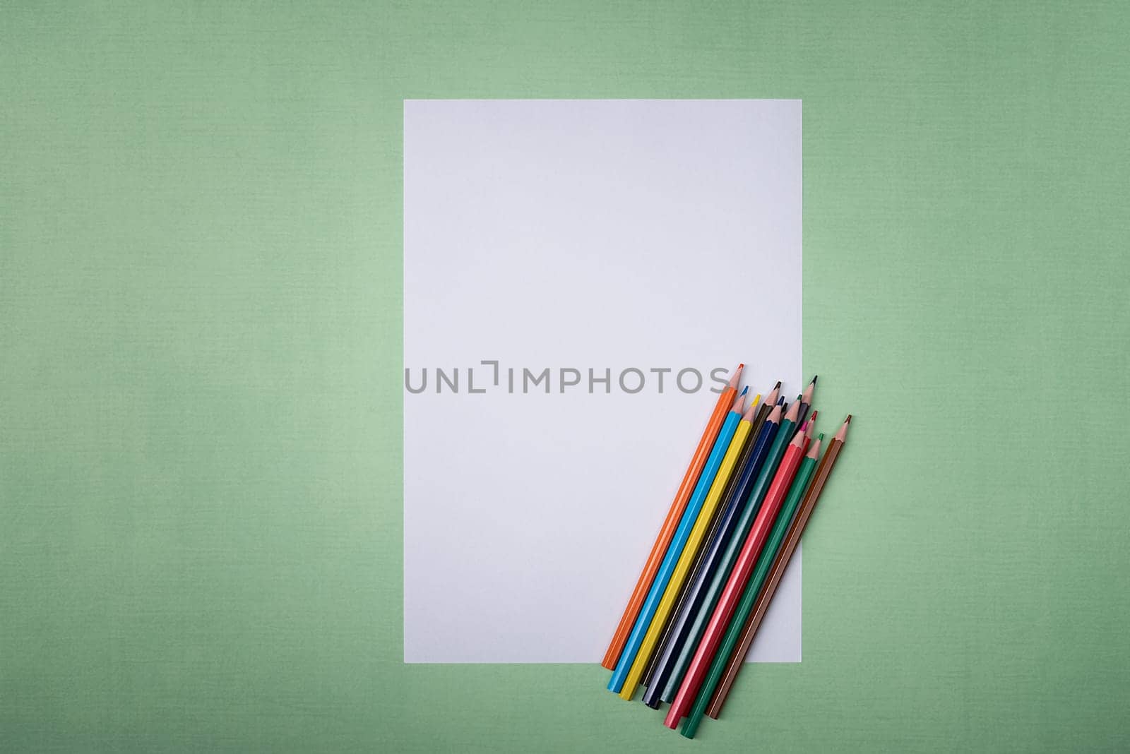A blank white sheet and colored pencils for drawing on a plain textured background with space for copying and lettering. Layout, mockup free space.