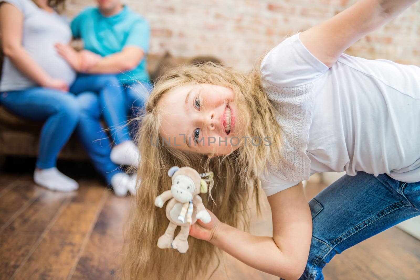 little girl fooling around in front of the camera, blurred family on the background