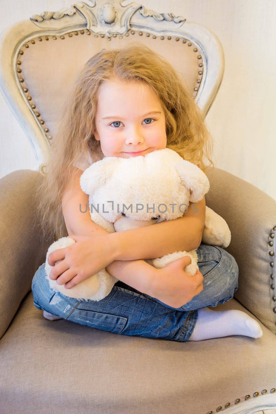 Cute girl in casual clothes sitting in the armchair and hugging toy