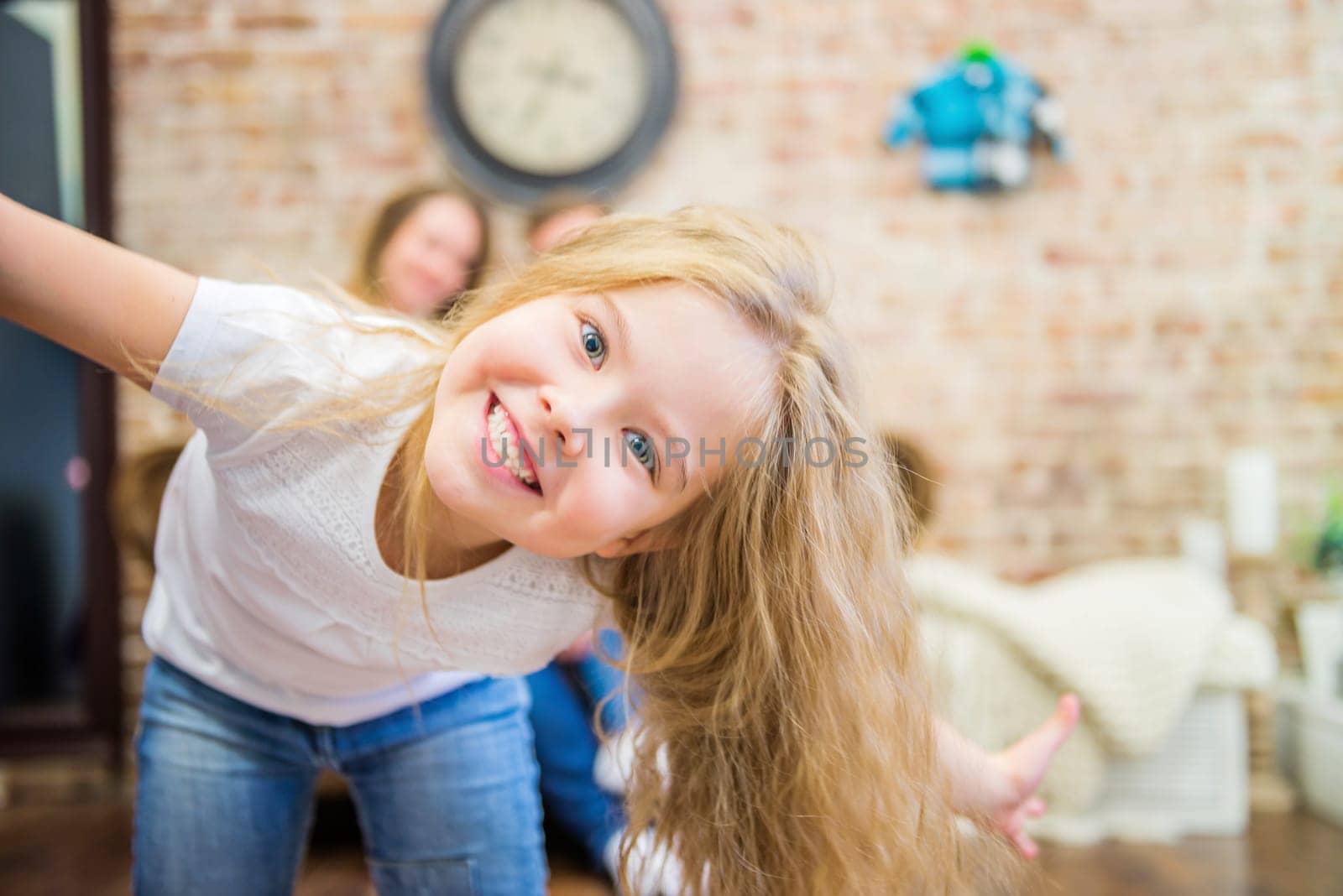 little girl fooling around in front of the camera, blurred family on the background