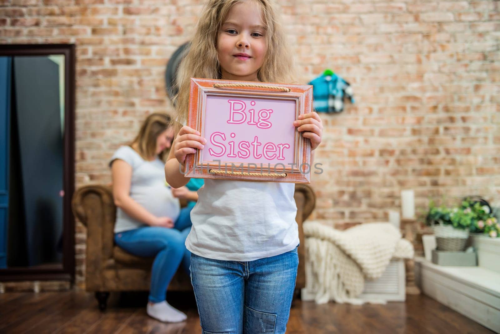 Cute girl in casual clothes standing and holding a sign with text, blurred family on the background