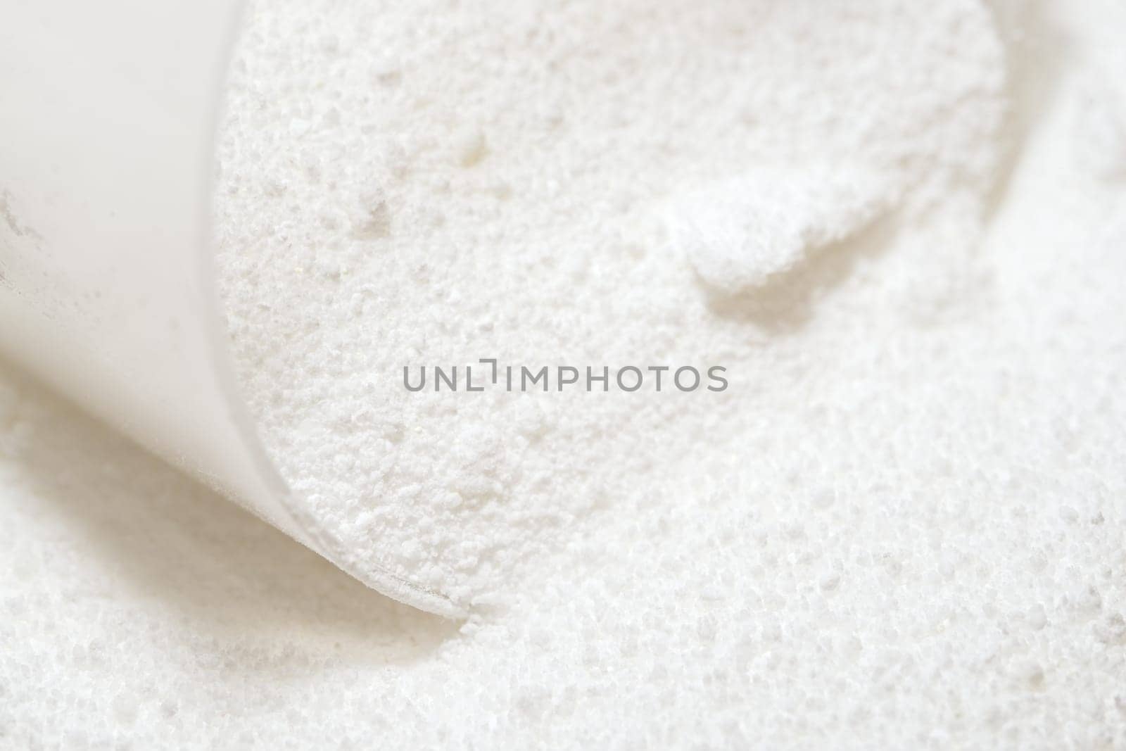 Macro image of clear plastic scoop measuring out white laundry detergent powder. Domestic cleaning chemical for clothing and fabrics.