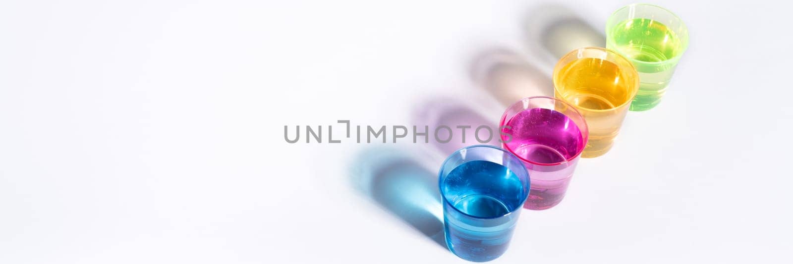 Plastic multi-colored glasses with liquid on a white background with highlights. Layout, mockup.