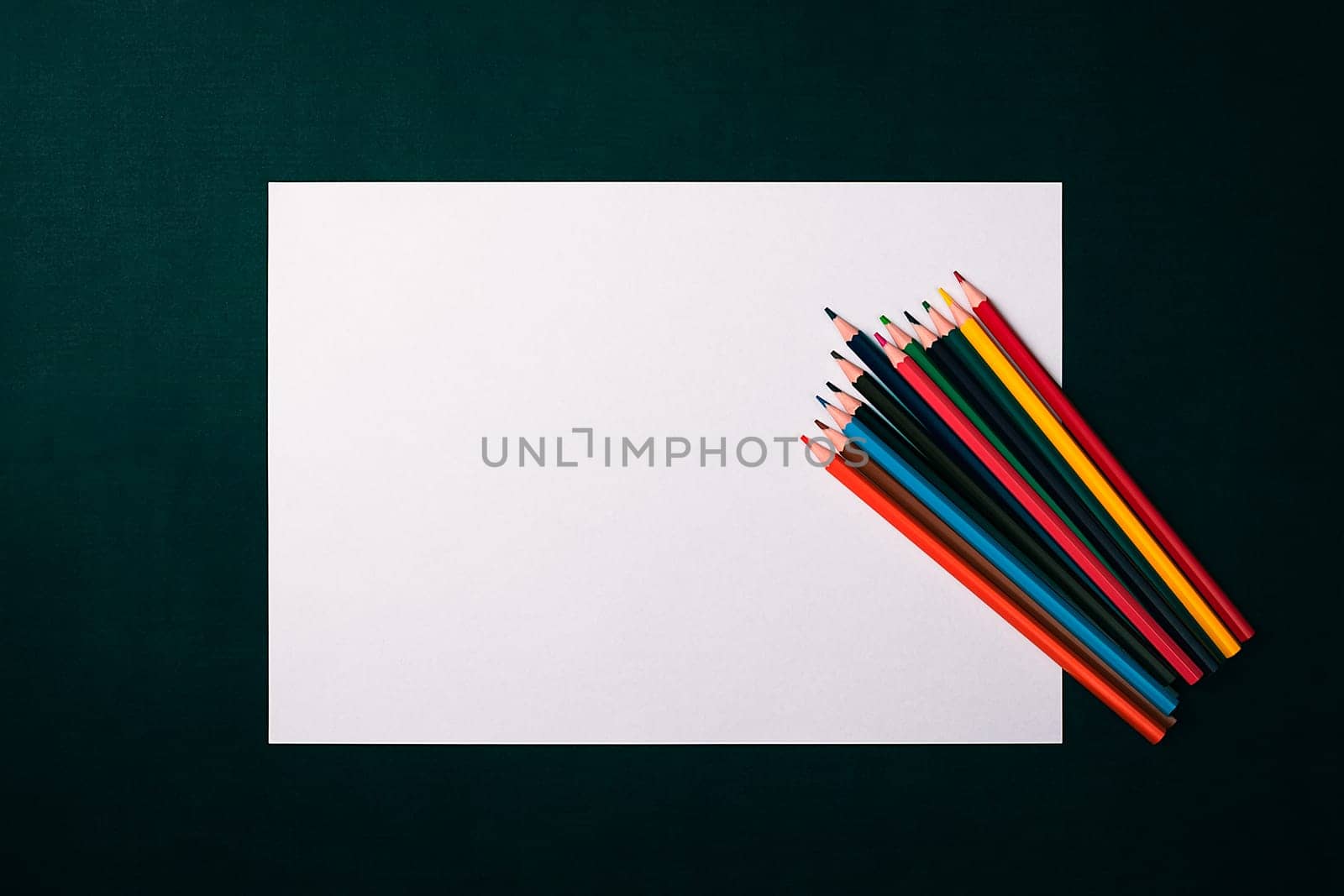 A blank white sheet and colored pencils for drawing on a plain textured background with space for copying and lettering. Layout, mockup free space.
