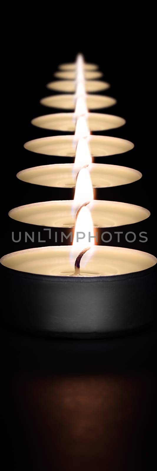 A row of burning candles on a dark background with a flare in the foreground. Layout, mockup.