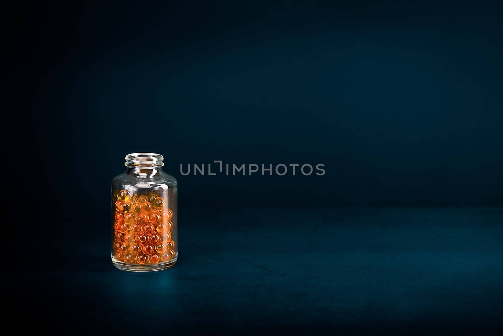 A glass jar with pills of bright orange yellow color on a blue background. Place for the label, logo, layout.