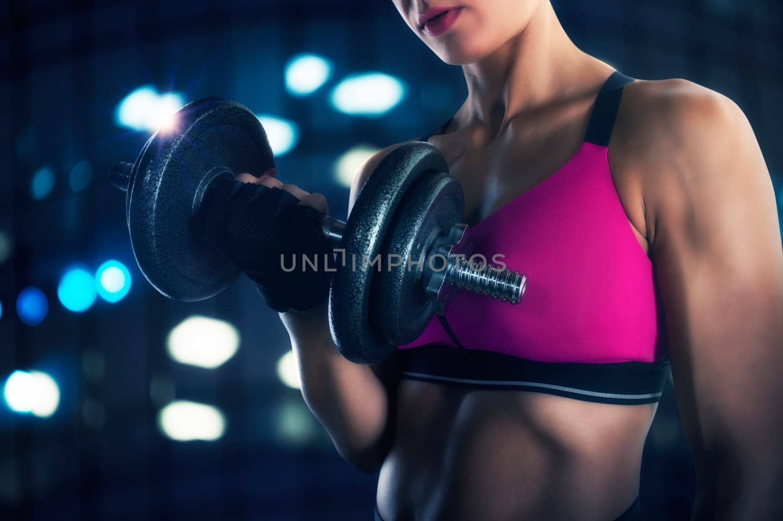 Athletic muscular woman training biceps with dumbbells at the gym