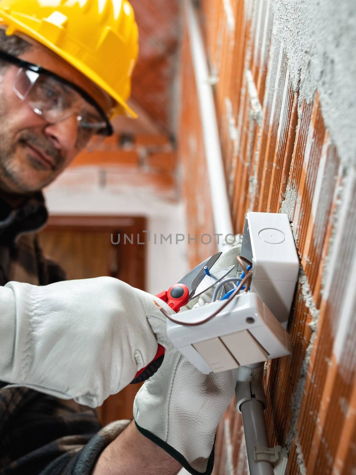 Electrician worker with scissors prepares the electrical cables of an electrical system  wear helmet, gloves and goggles. Workplace safety.