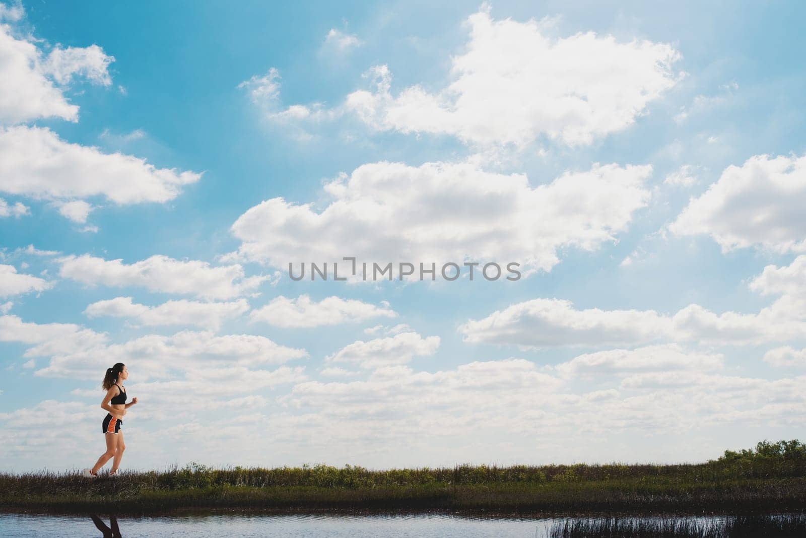 Sporty woman runs on a green field during a sunny day
