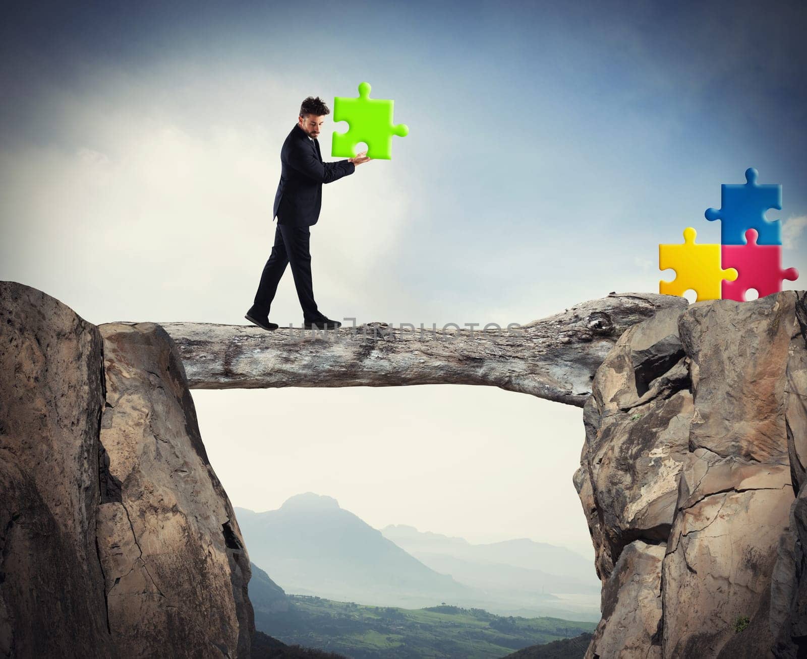 Businessman carries a piece of puzzle while he walking on a tree trunk between the mountains. concept of missing piece