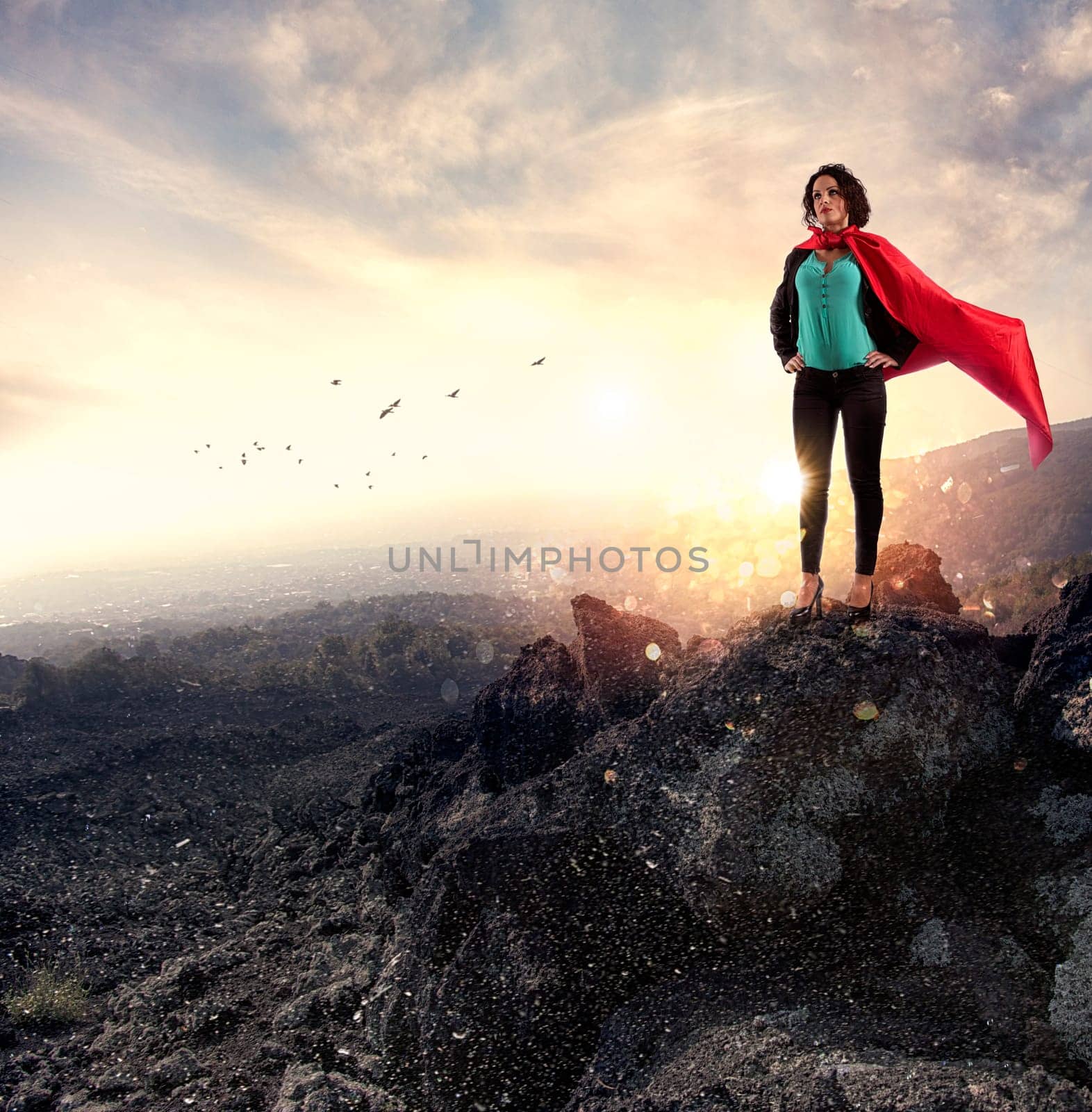 Successful businesswoman acts like a super hero on a mountain during sunrise. Concept of determination and success