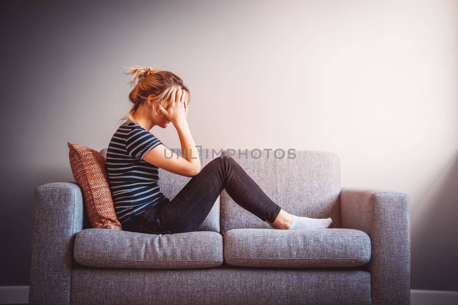 Depressed woman sitting on the couch at home. Concept of the quarantine, job loss and family's problems.