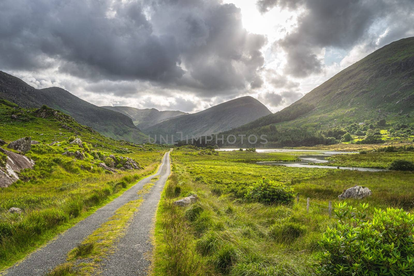 Straight country road leading trough Black Valley, dramatic sky. Landscape with lake, river and MacGillycuddys Reeks mountains, Ring of Kerry, Ireland