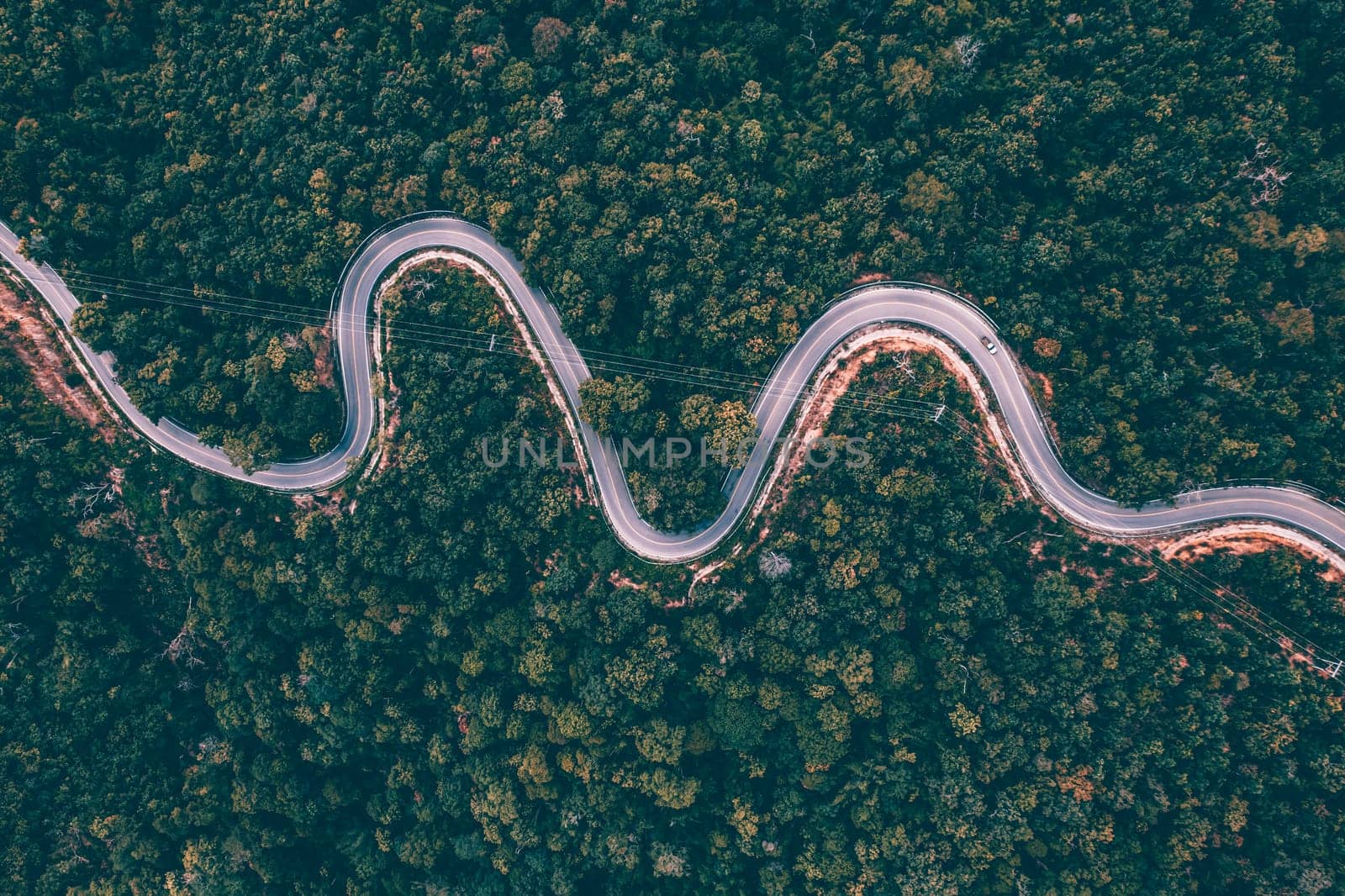 Aerial view of countryside road passing through the green forrest and mountain.