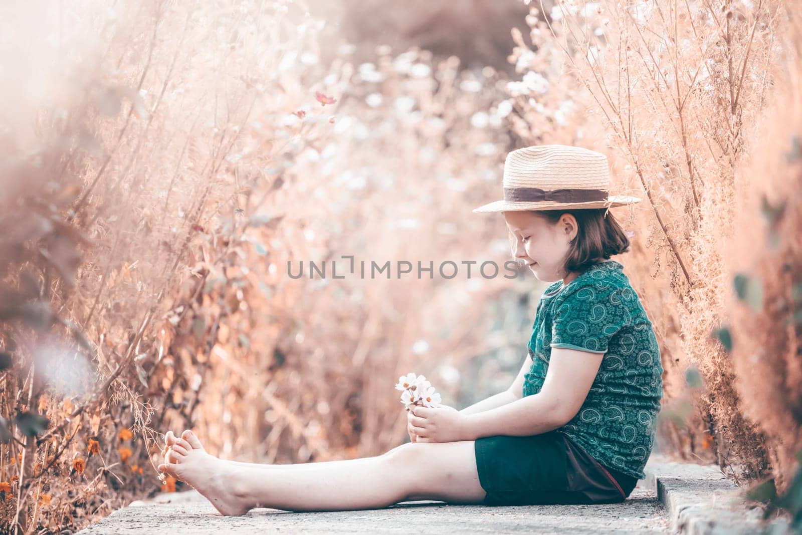 Little adorable girl sitting in colorful flower garden enjoying autumn sunlight.