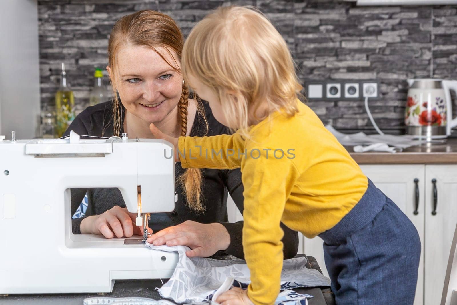 Smiling young mother is sewing with her cute son together. Horizontally.