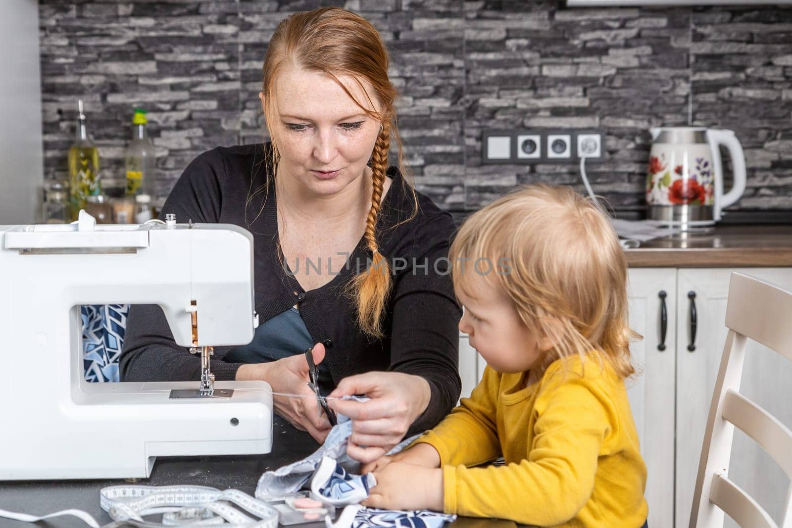 Little boy watches his young mother. She is cuting the fabric. Horizontally.