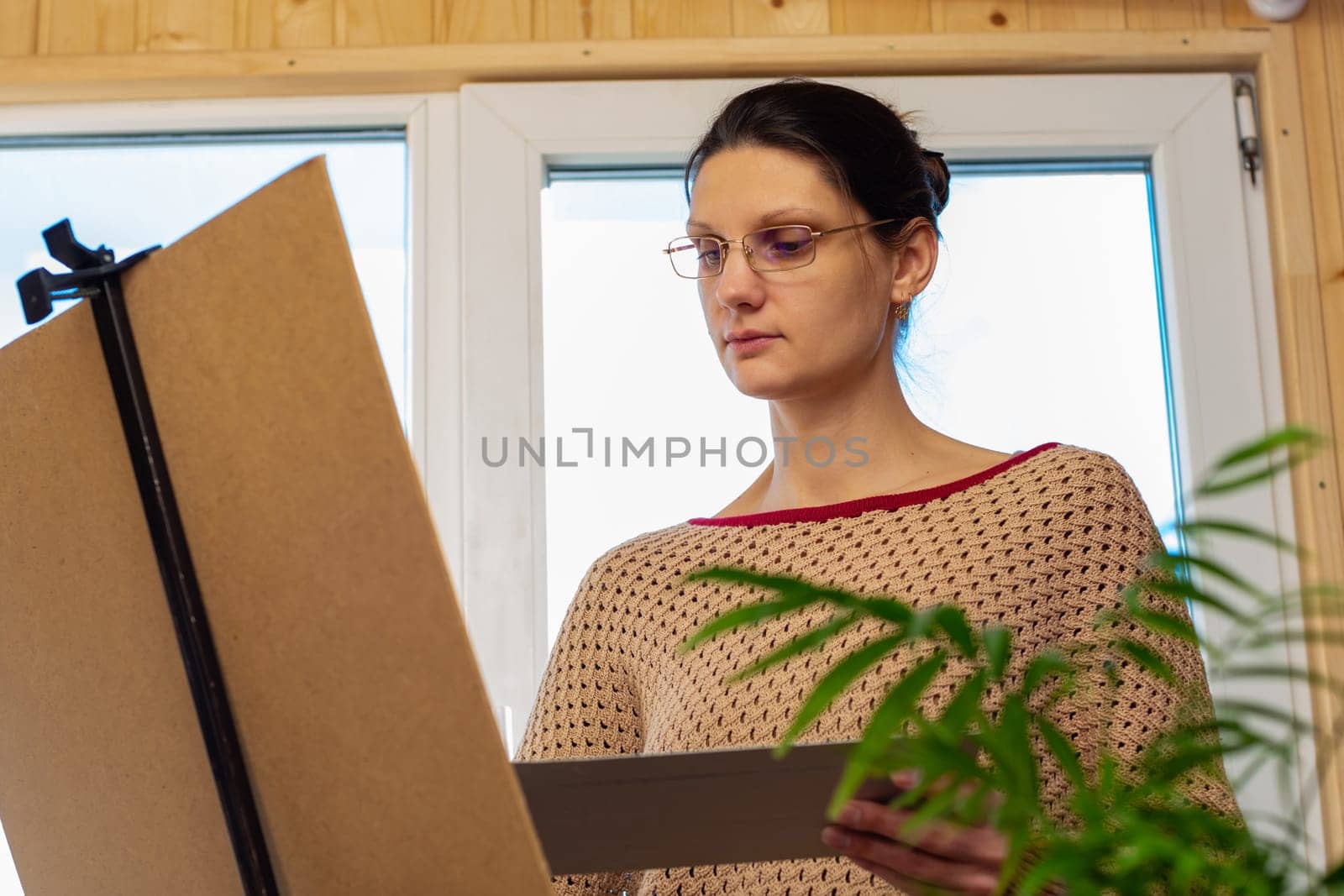 Portrait of an artist at work, a girl draws a drawing on an easel by the window