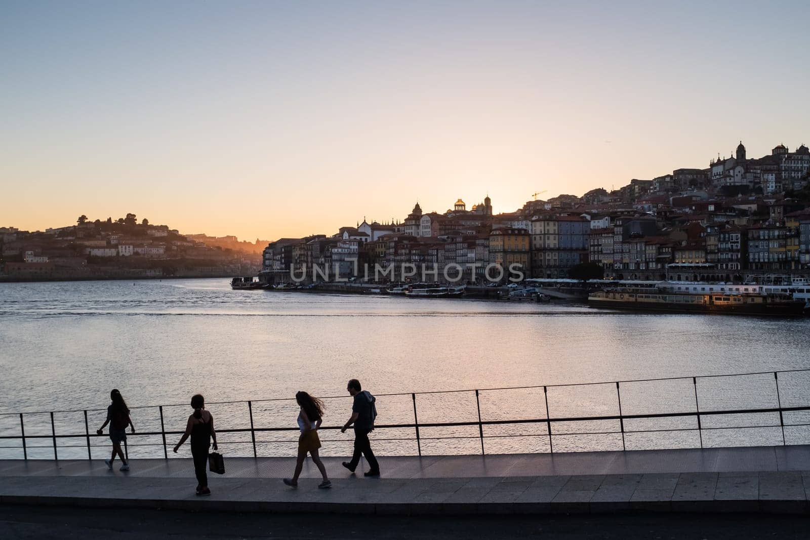 Silhouette family of four who walking along avenue with views over River Douro and Porto cityscape at sunset.