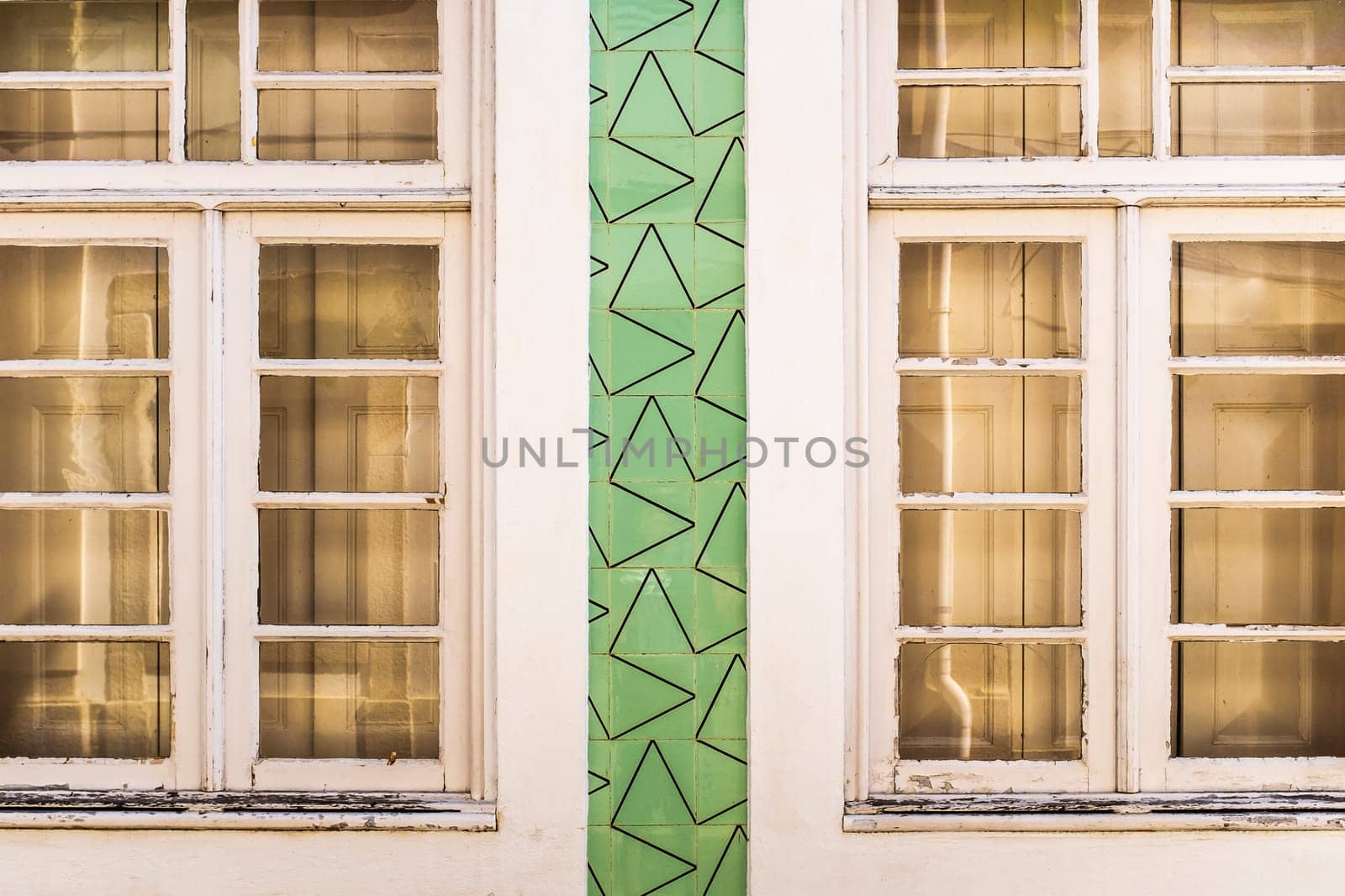 Facade of an old house in Aveiro (Portugal) with white wooden windows decorated by Portuguese tiles in green with geometric unusual pattern. Close up front view.