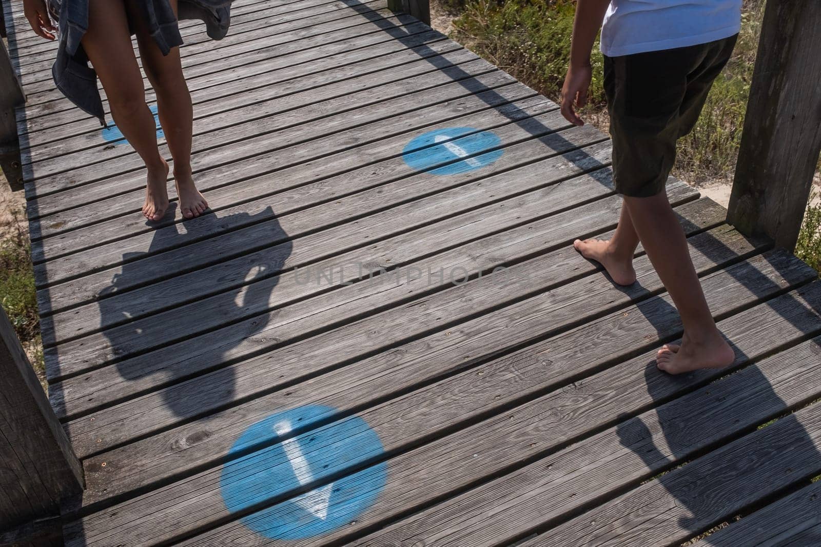 Two children are walking on the wooden walkway following the instructions for the social distancing: circle to the right and avoid stopping. Costa Nova do Prado, a Portuguese seaside resort located in Aveiro District.