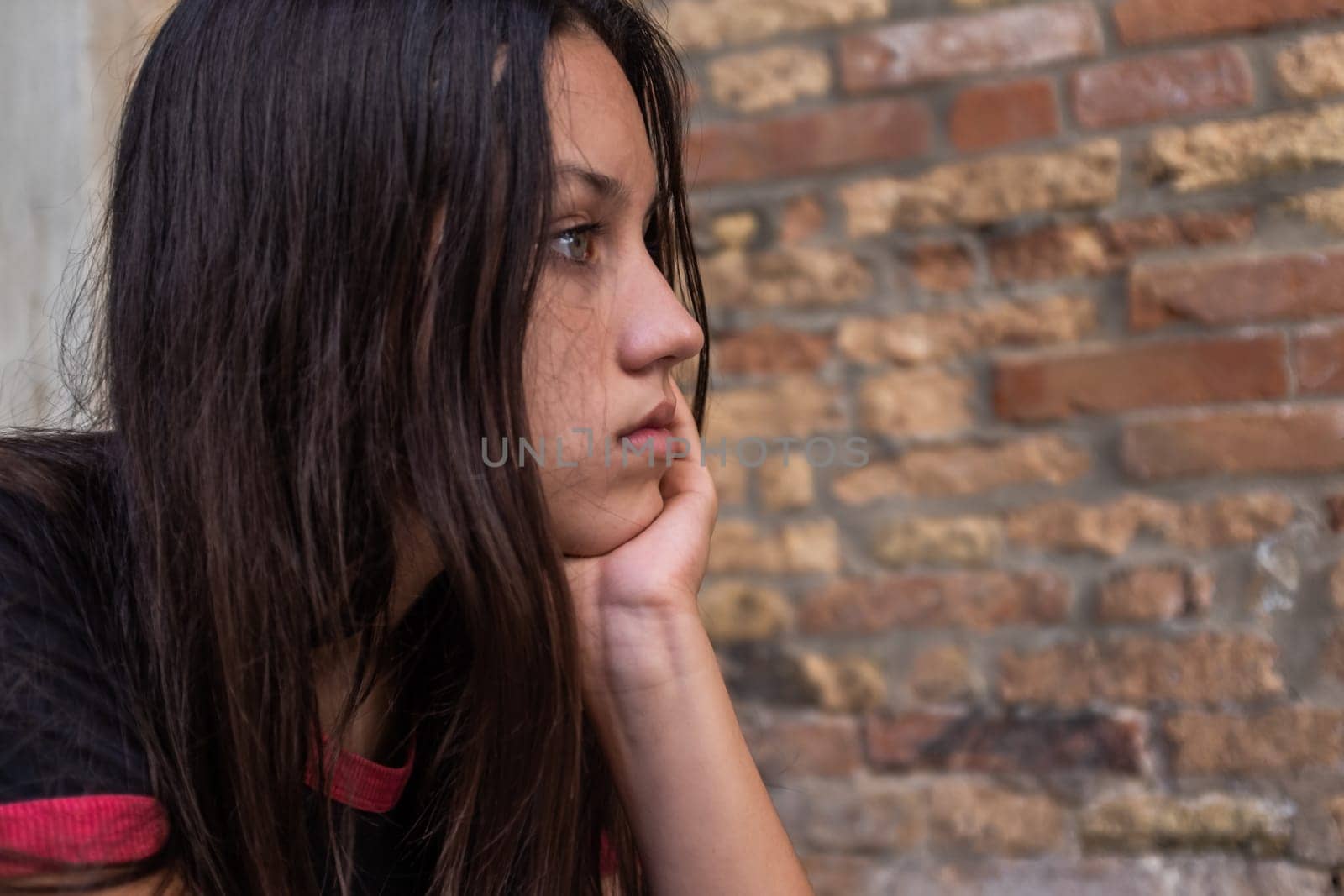 Portrait of beautiful brown hair girl holding chin with hand thinking about emotional problems and looking away, profile view, copy space.