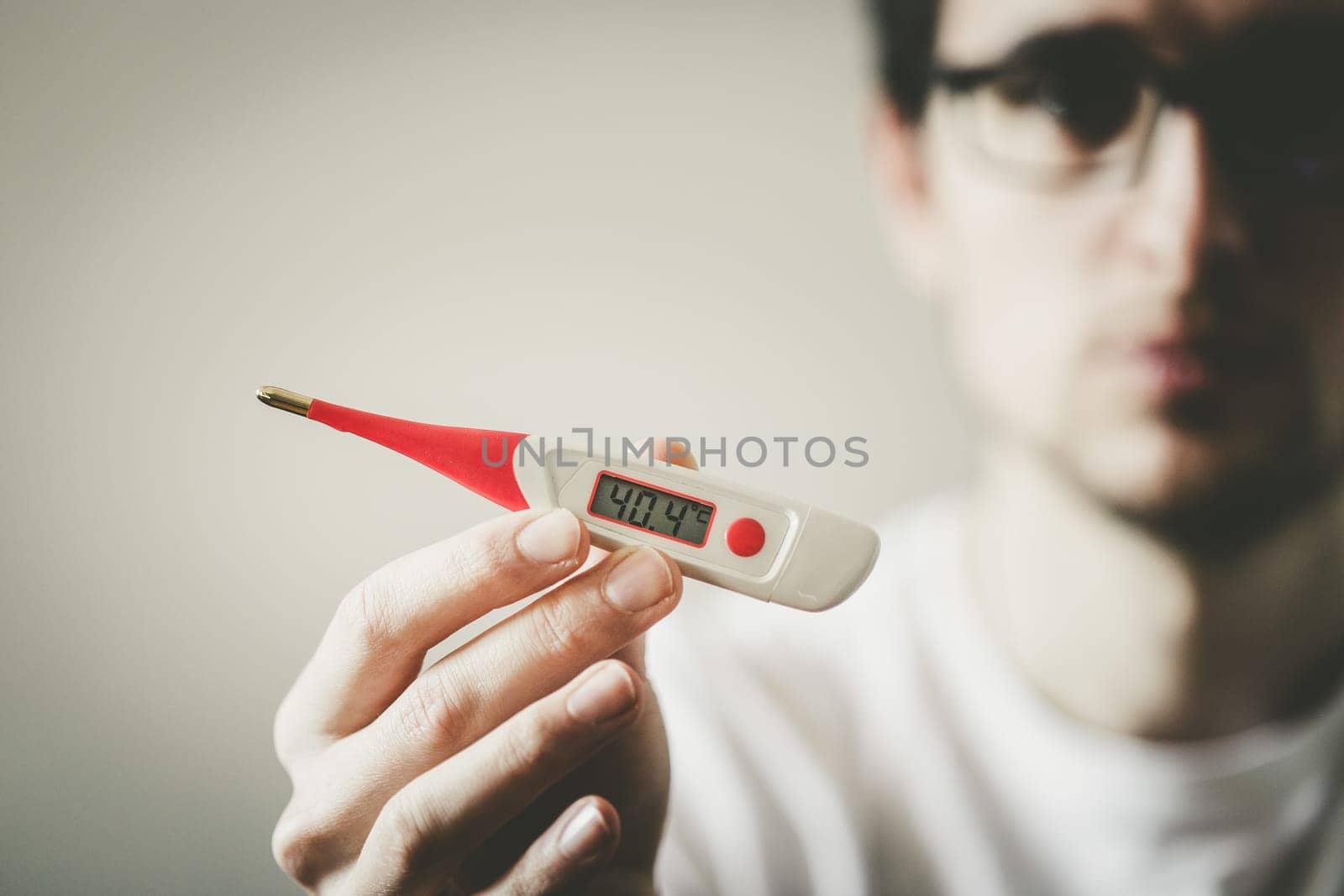 Man holds a red fever thermometer with high temperature in his hand, blurry face