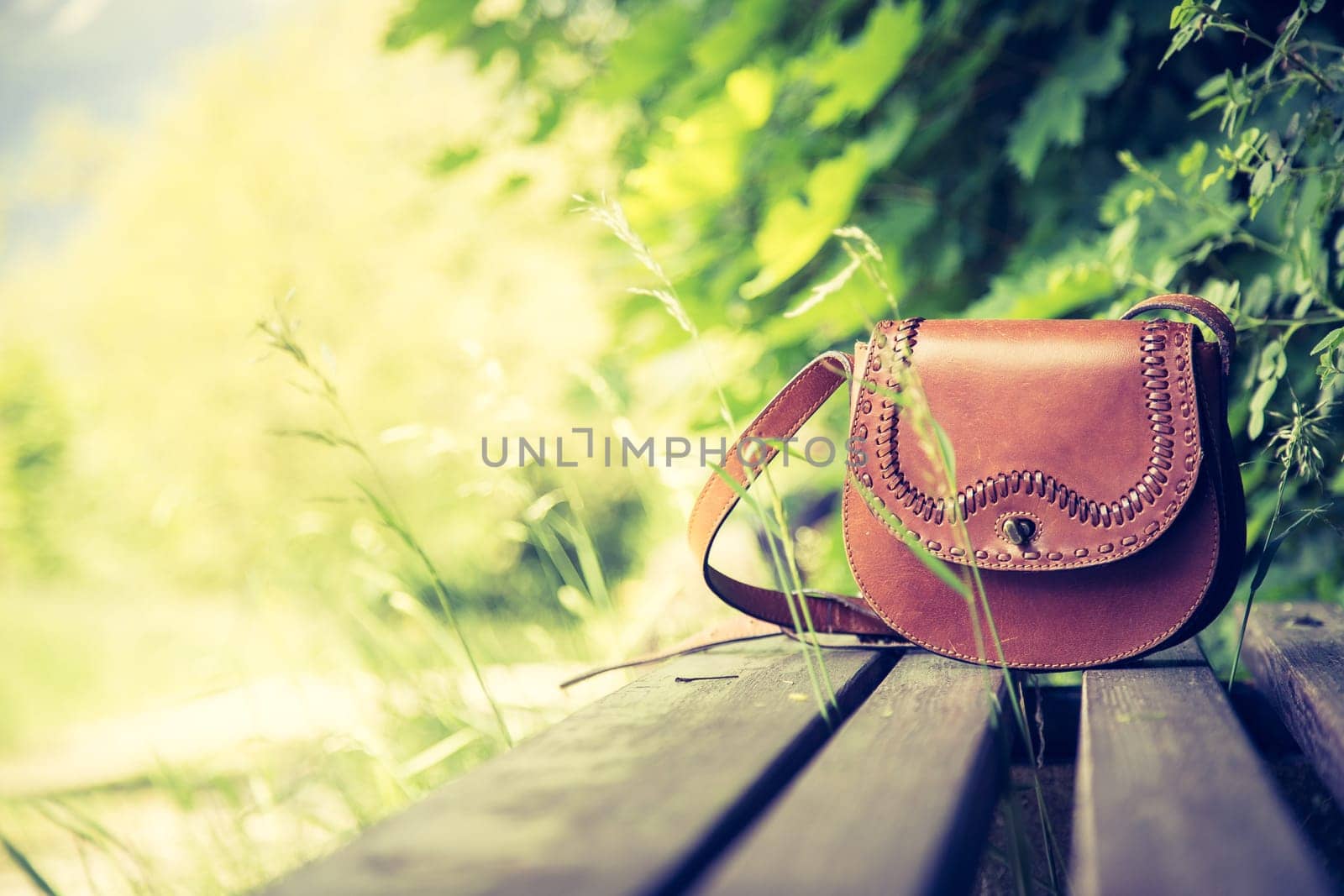 Leather hand bag lies on a wooden park bench, summer time, nobody
