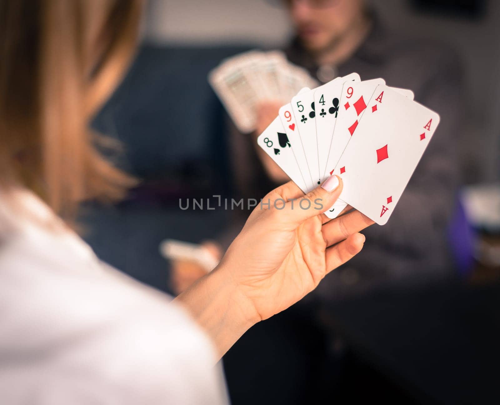 Card playing at home: Friends are sitting on a table. Woman playing cards, man in blurry background.