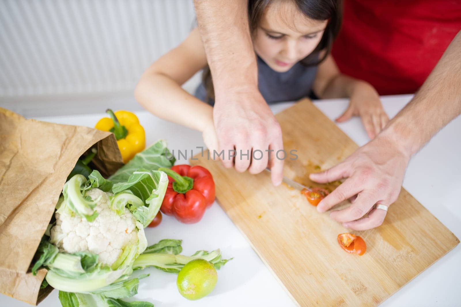 Little girl and her father slicing lemons, tomatoes, and bell peppers on cutting board. Male hands and young child cutting vegetables on wooden board. Daughter-father cooking together