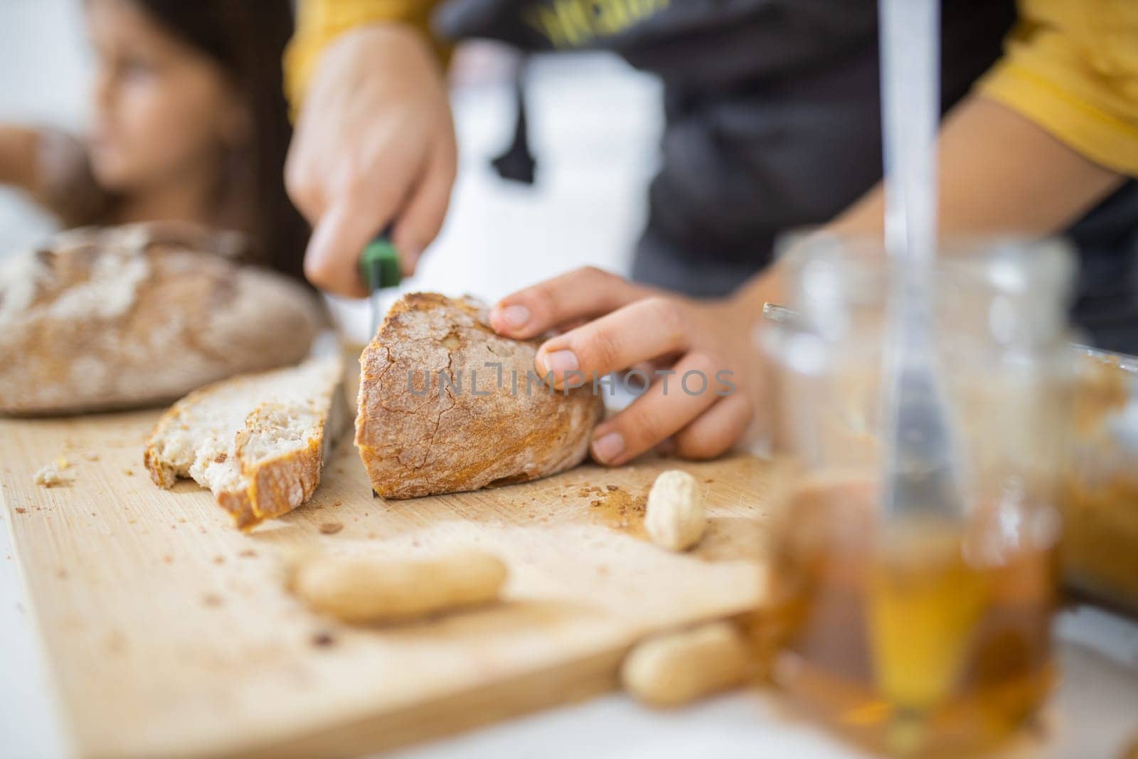Female hands slicing bread on wooden cutting board. Woman cutting sourdough bread next to honey jar. Healthy meal preparation