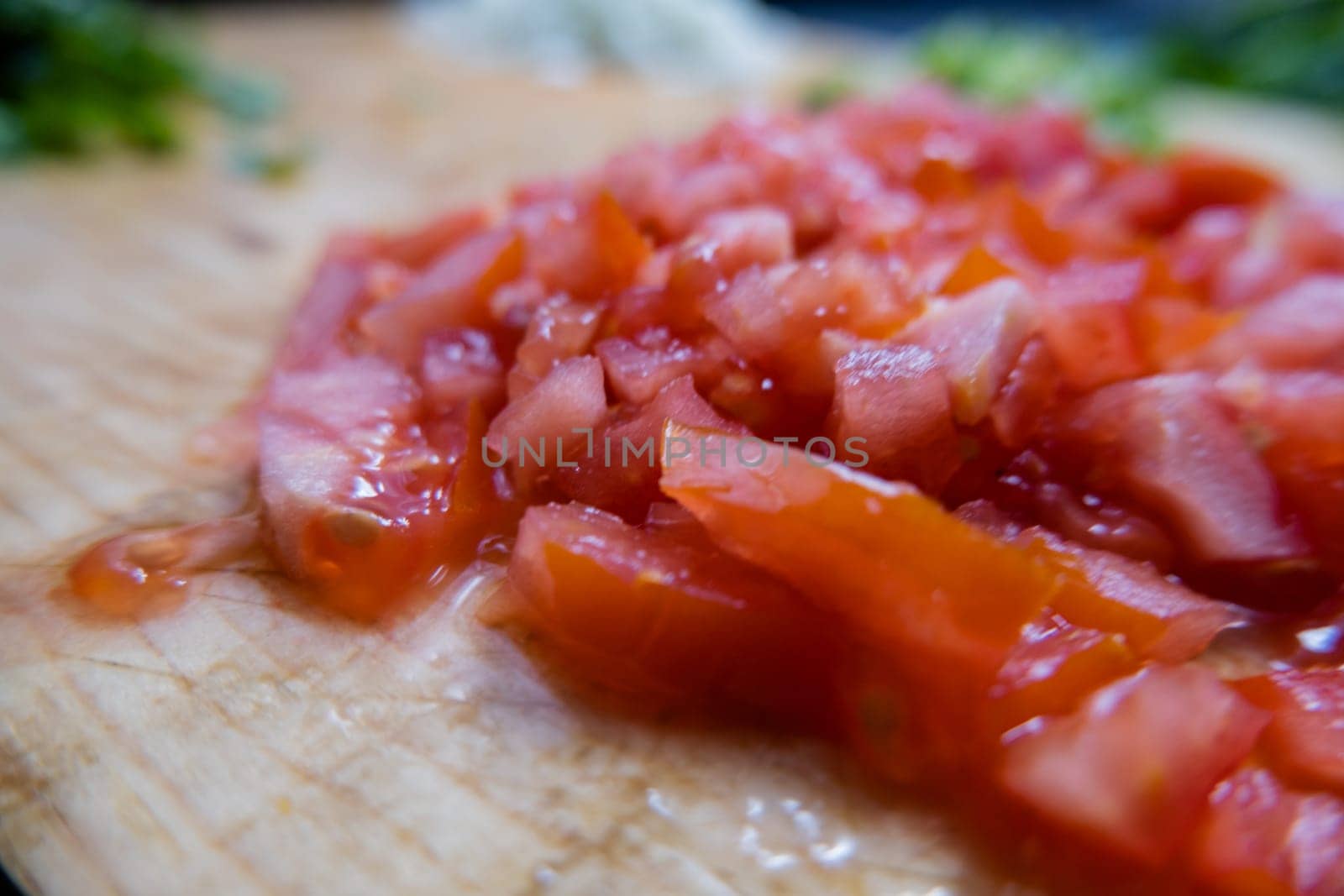 Close-up of fresh chopped tomatoes on wooden cutting table with chili pepper slices as background. Juicy red vegetables cut into pieces above wood surface. Healthy snack preparation