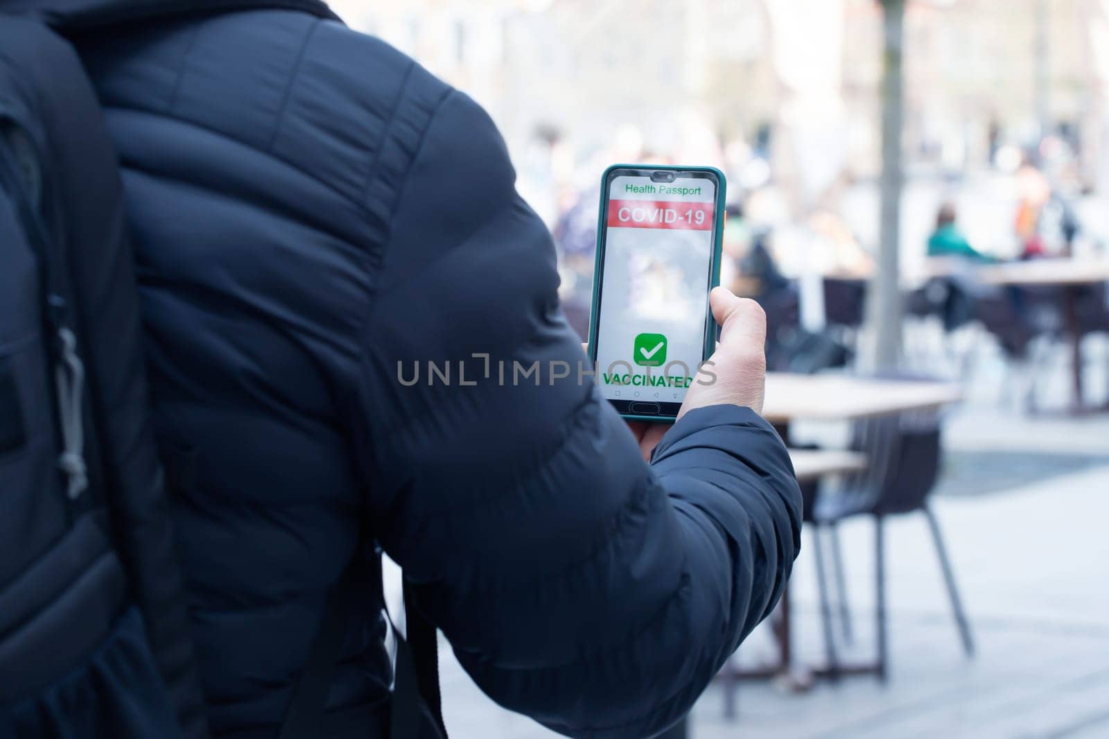 Vaccinated person using immunization certificate on smartphone at the restaurant or terrace.