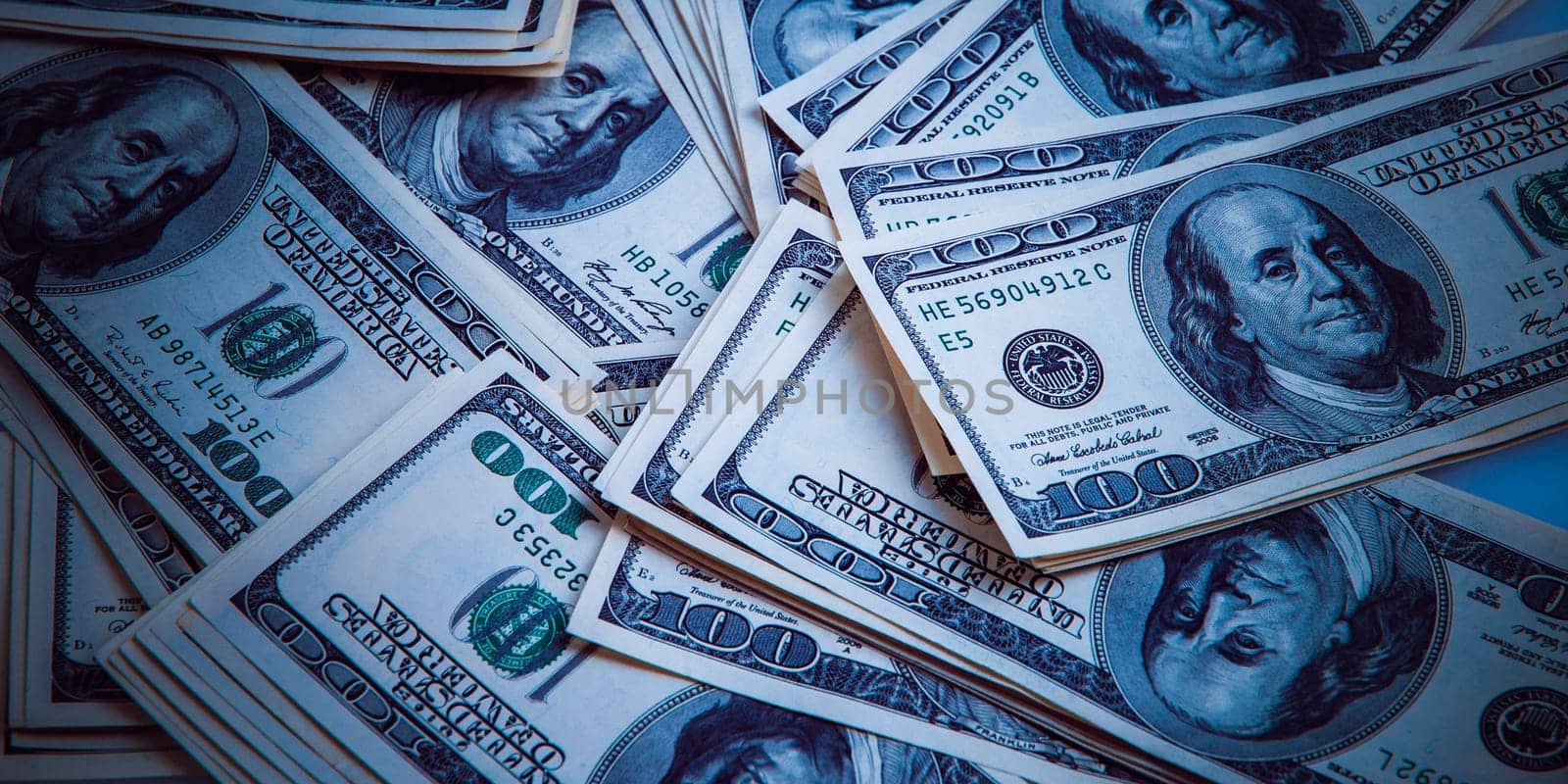 Cash of hundred dollar bills, dollar background image. One hundred US banknotes are scattered over the background. Style blue color and vignetting.
